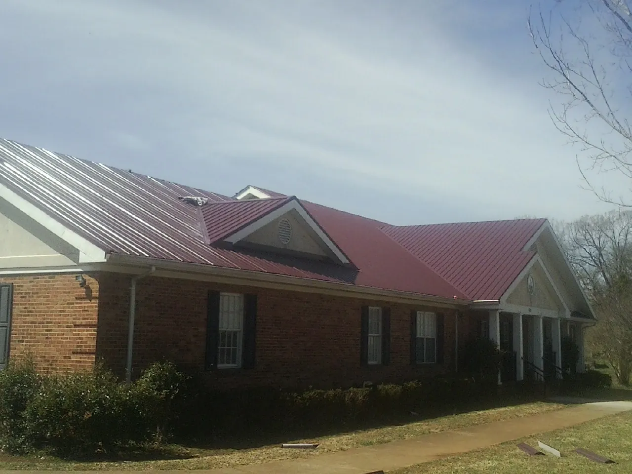 Red metal roof with gabled entries on a long brick building, from a Hail Damage Roof Repair job in Ware Shoals