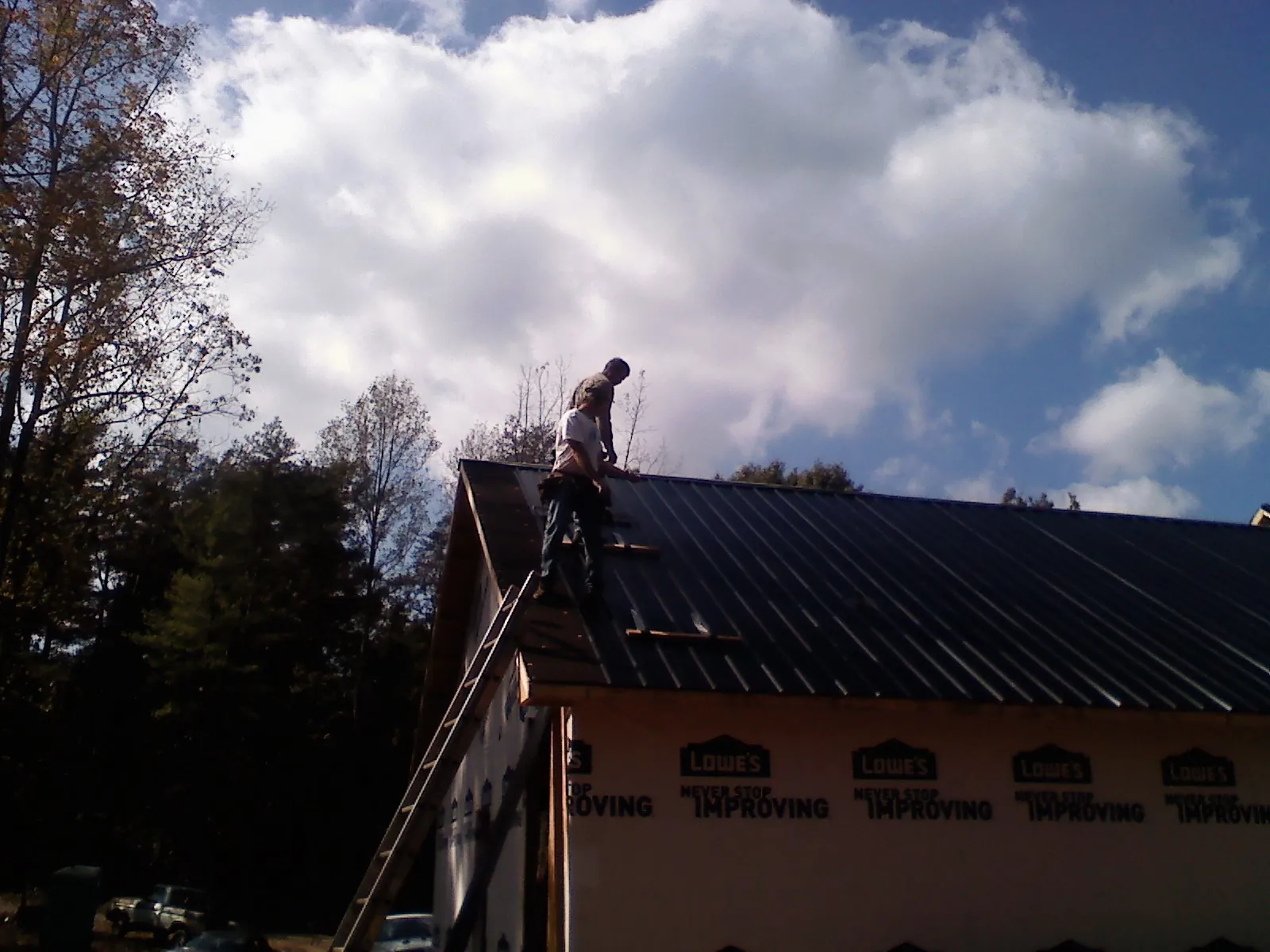Roofer fastening dark metal panels high against a cloudy sky, from a Roof Inspection job in Ware Shoals